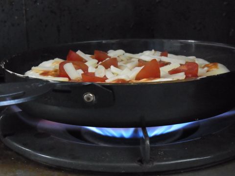 ピザ生地にケチャップを塗り、ミニトマトとチーズをたっぷりのせて、まずはコンロで下面を焼きます。
