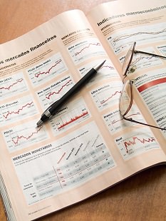 各国の株価指数チャートが載った本の上のペンと眼鏡